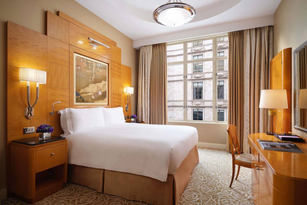 Habitación de hotel con una cama grande, dos l ámparas de noche, un escritorio con silla, un ventanal con cortinas y un cuadro en la pared.
