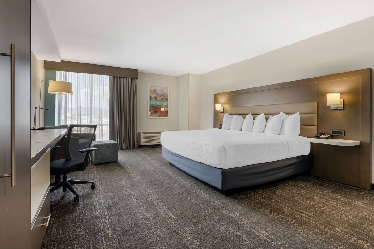 A hotel room with a large bed, a desk with a chair, a lamp, and a painting on the wall.