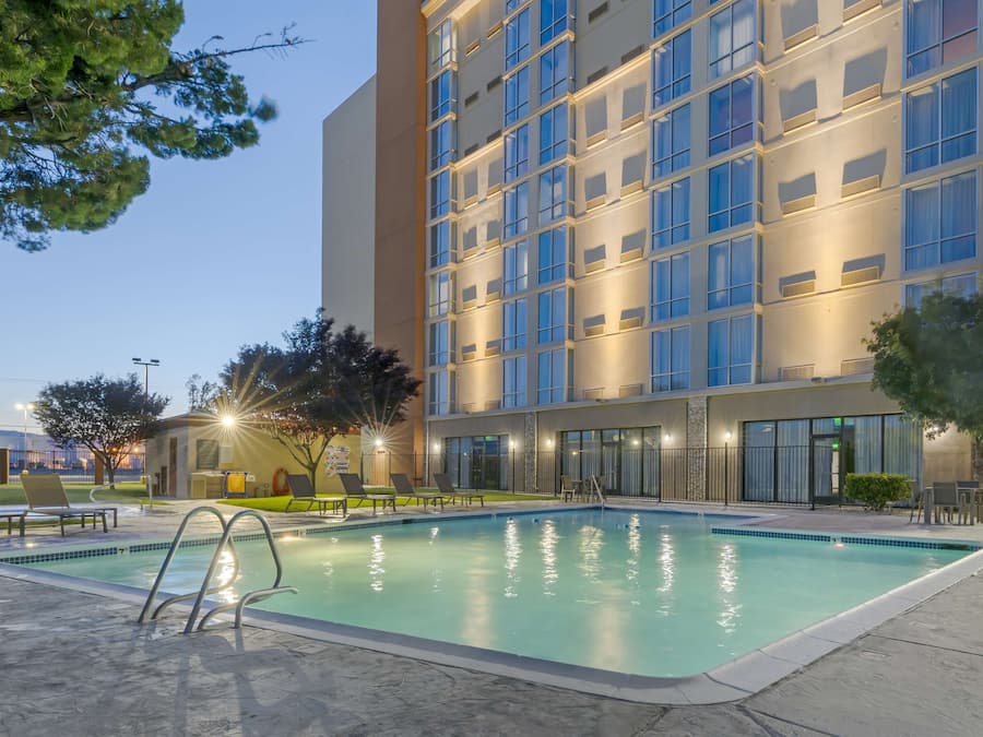 Un hotel moderno con piscina, sillones de descanso y fachada bien iluminada.