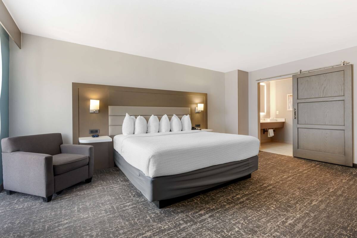 A hotel room with a large bed, a chair, a bedside table, and a wardrobe.