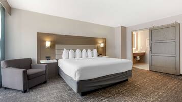 A hotel room with a large bed, a chair, a bedside table, and a wardrobe.