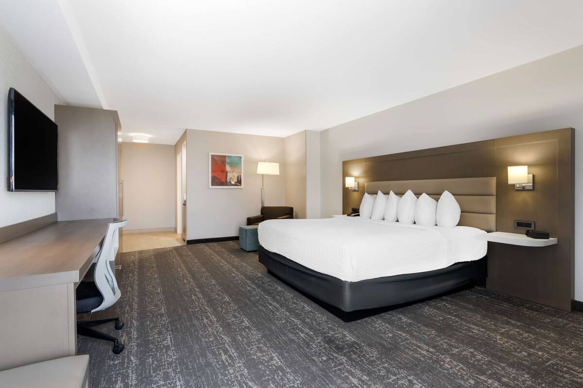 A hotel room with a large bed, a desk with a chair, a flat-screen TV, and a painting on the wall.