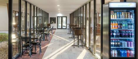 A corridor with glass walls, a vending machine, and seating areas.