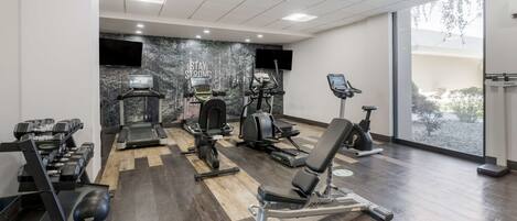A gym with treadmills, weight machines, and a TV screen.