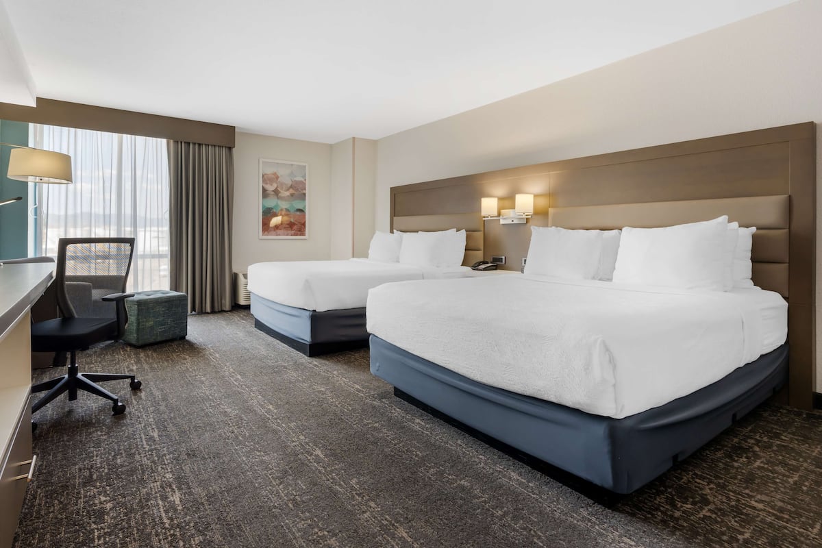 A hotel room with two beds, a desk, a chair, a lamp, and a painting on the wall.