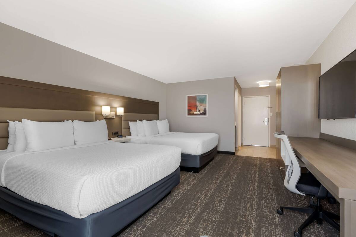 A hotel room with two beds, a desk, a chair, a TV, and a painting on the wall.