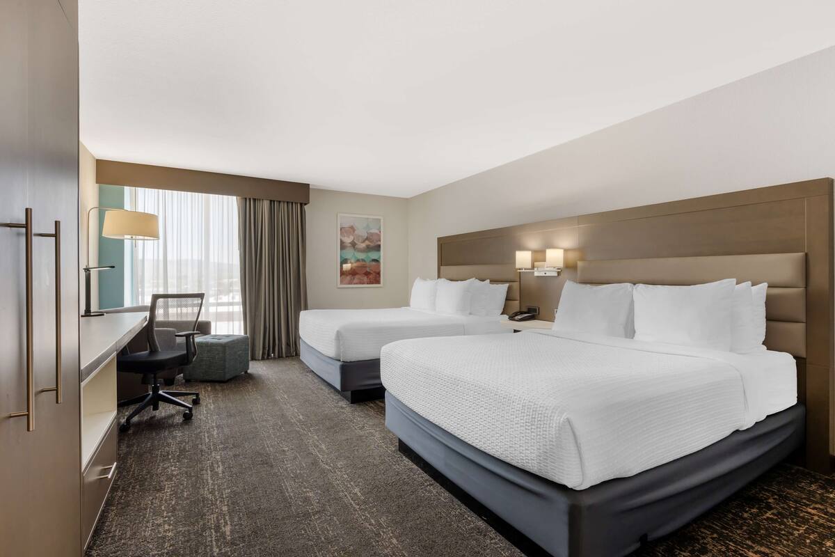 A hotel room with two beds, a desk, a chair, and a window with curtains.