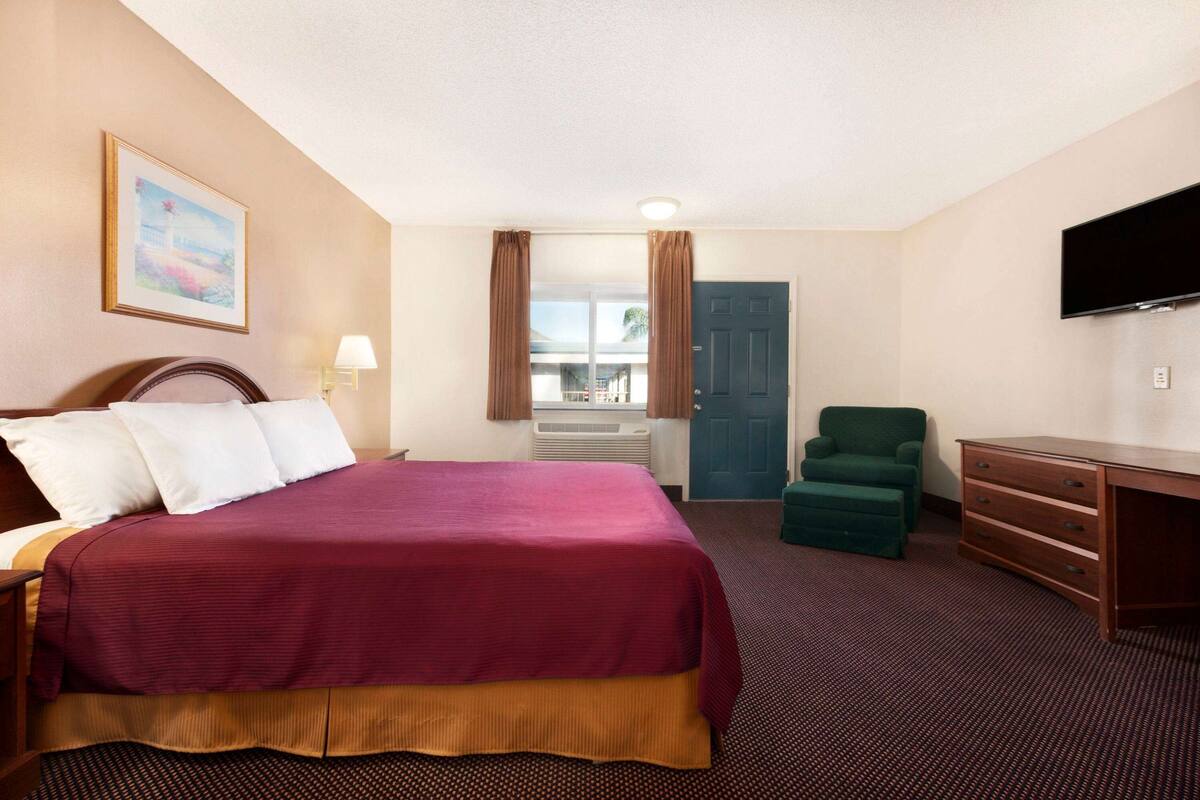 A hotel room with a large bed, a desk, a chair, a television, and a window with curtains.