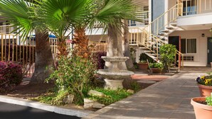 A courtyard with palm trees, a stone fountain, and a building with a staircase. - Travelodge by Wyndham Bakersfield (Bakersfield)