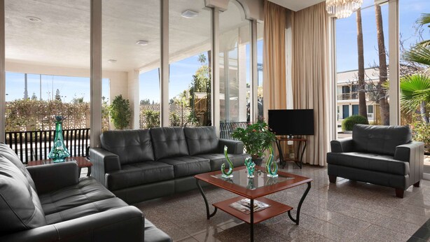 A spacious living area with a leather sofa, a coffee table, and a TV. - Travelodge by Wyndham Bakersfield (Bakersfield)