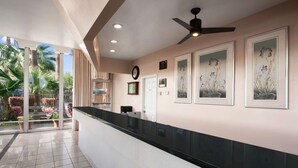 A hotel reception area with a black counter, ceiling fan, framed artwork, and a view of the outdoor garden. - Travelodge by Wyndham Bakersfield (Bakersfield)