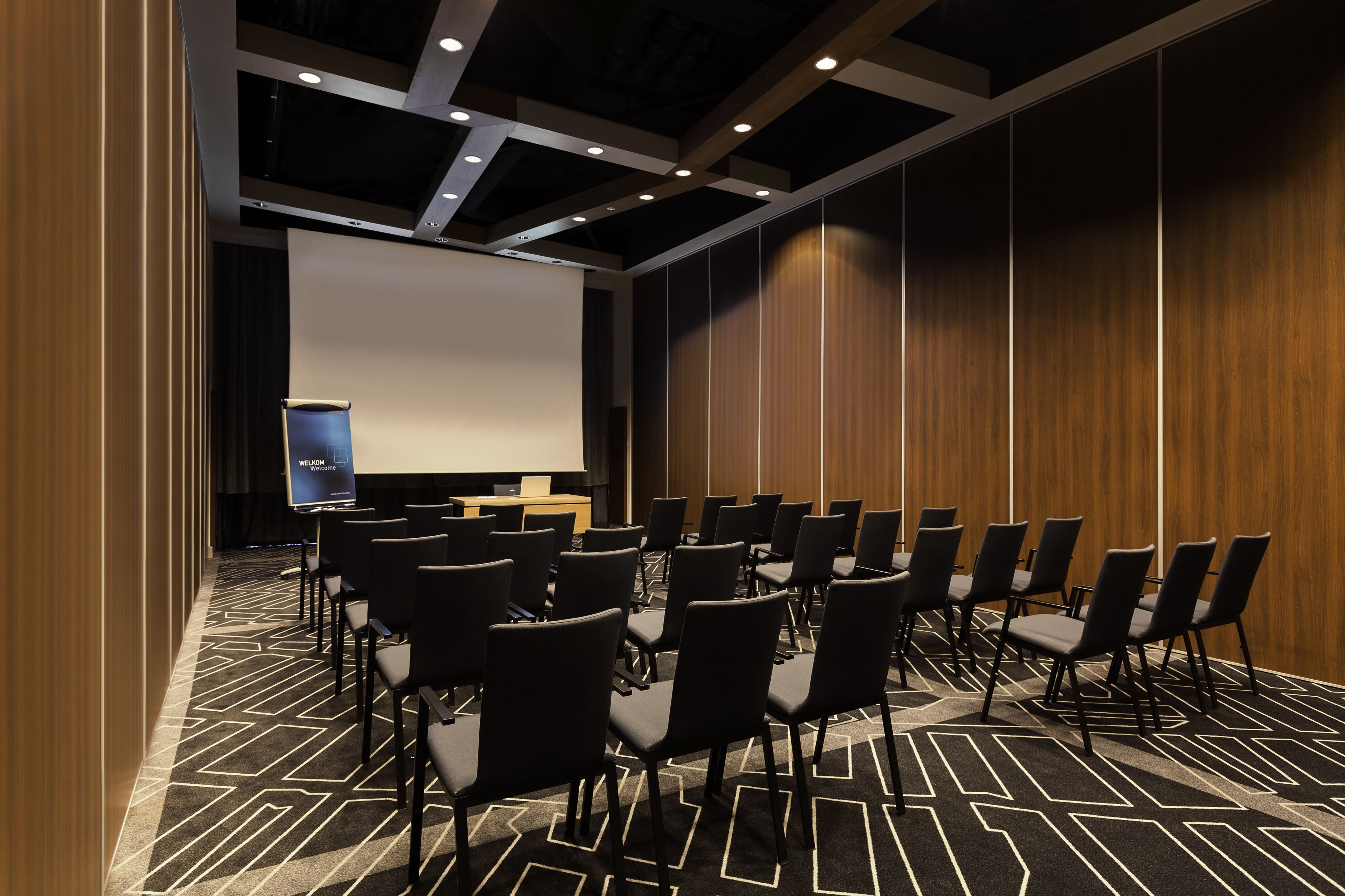 Un salón de conferencias con filas de sillas, un atril y una pantalla grande.