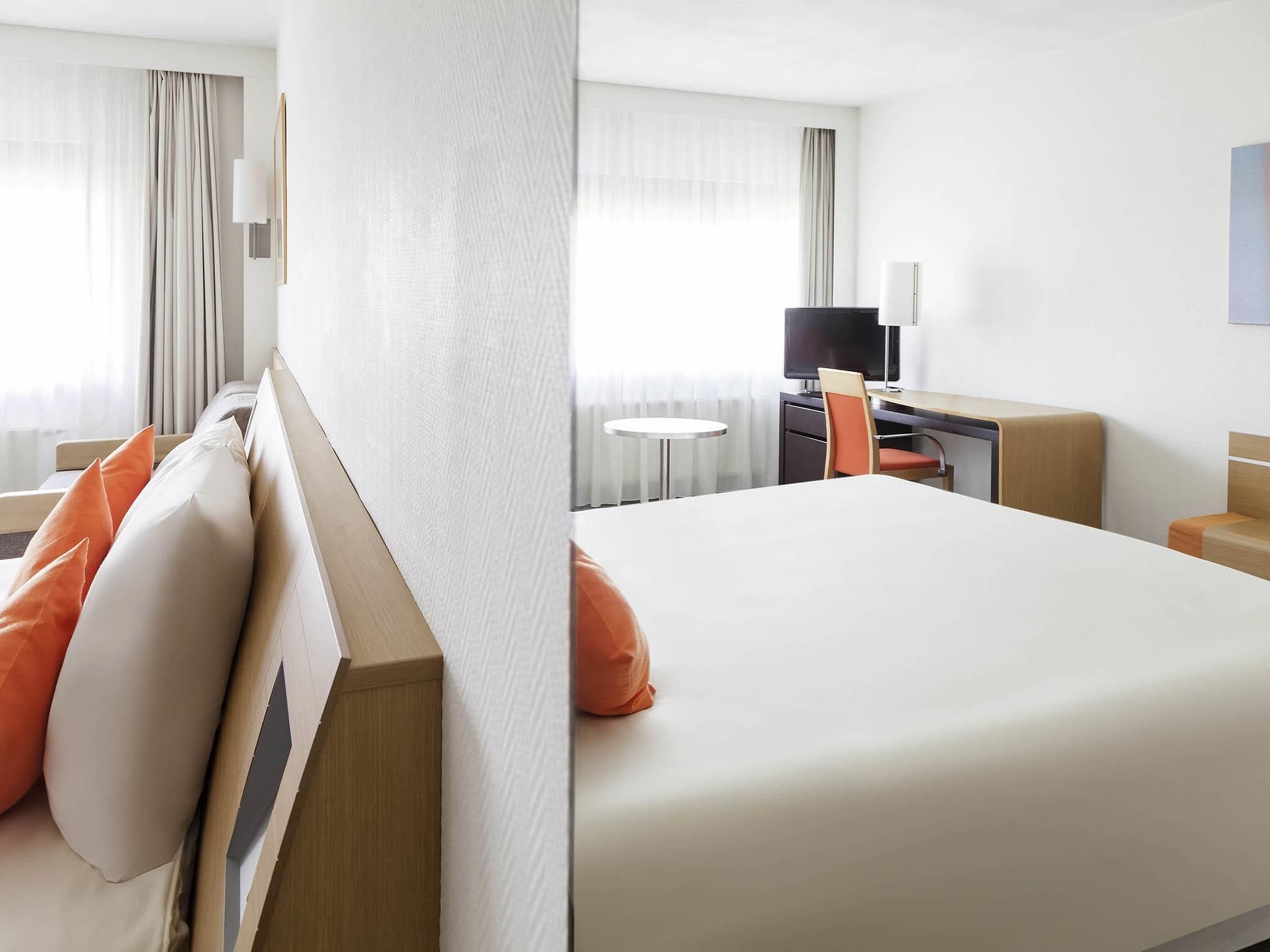 Quarto de hotel com cama, escrivaninha, cadeira, televisão e janela com cortinas.