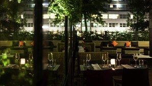An outdoor dining area with tables set for two, each with a candle and wine glasses.