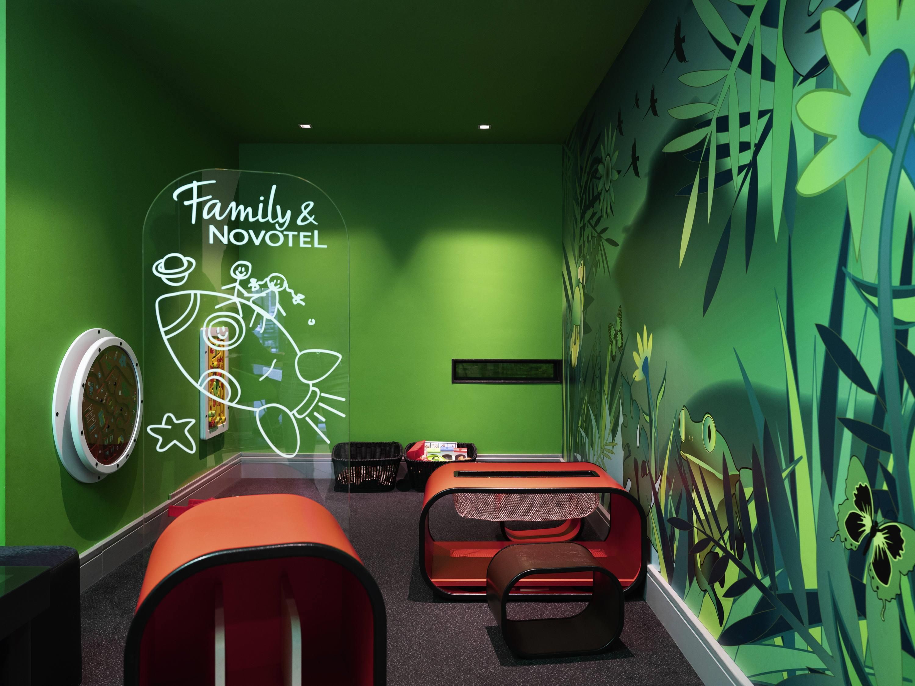 Habitación ideal para familias, con paredes verdes, un mural y un letrero de neón que dice 'Family & Novotel'.