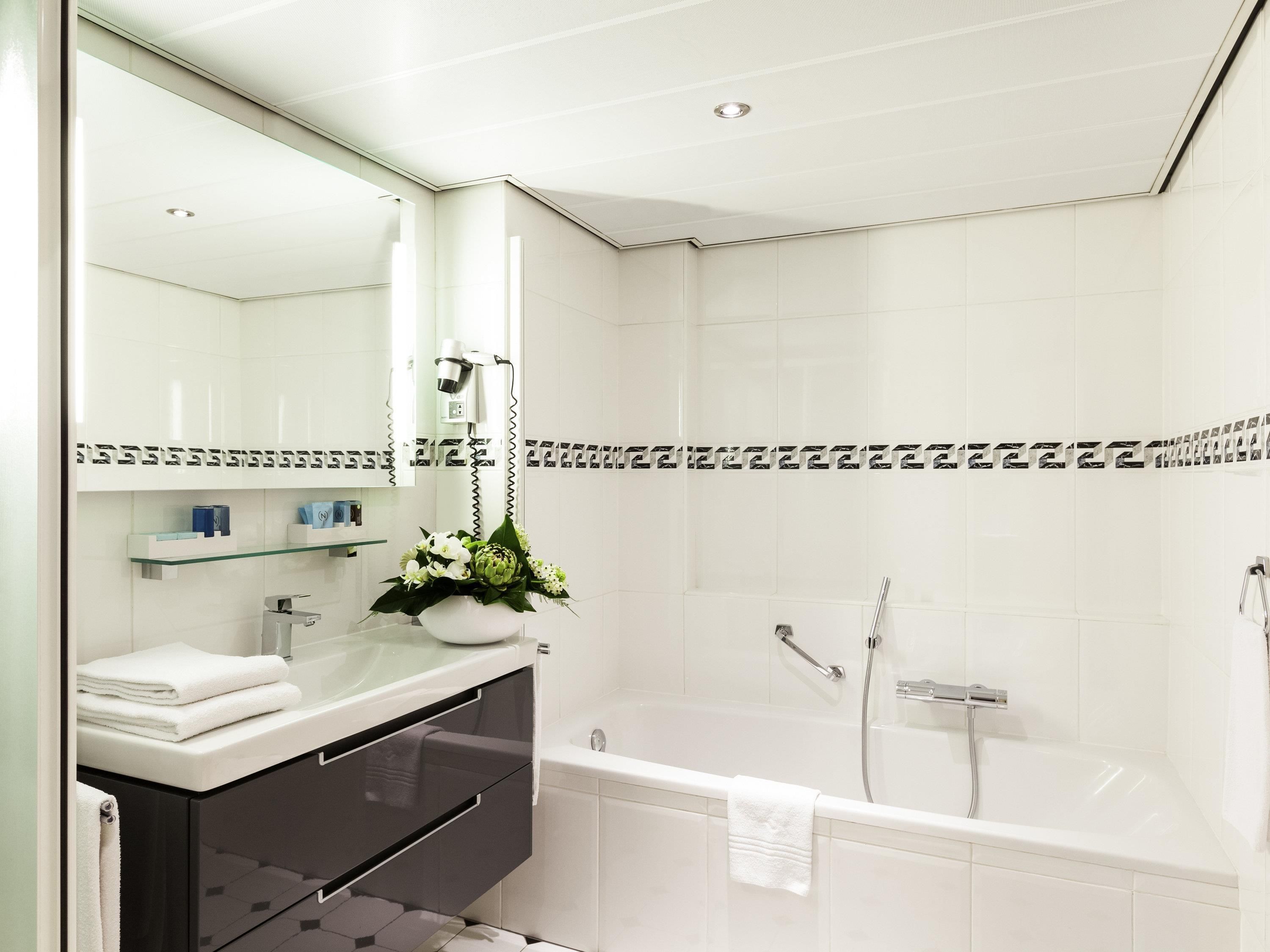A modern bathroom with a white sink, mirror, and vanity, a shower with a handheld showerhead, and a towel hanging on the wall.
