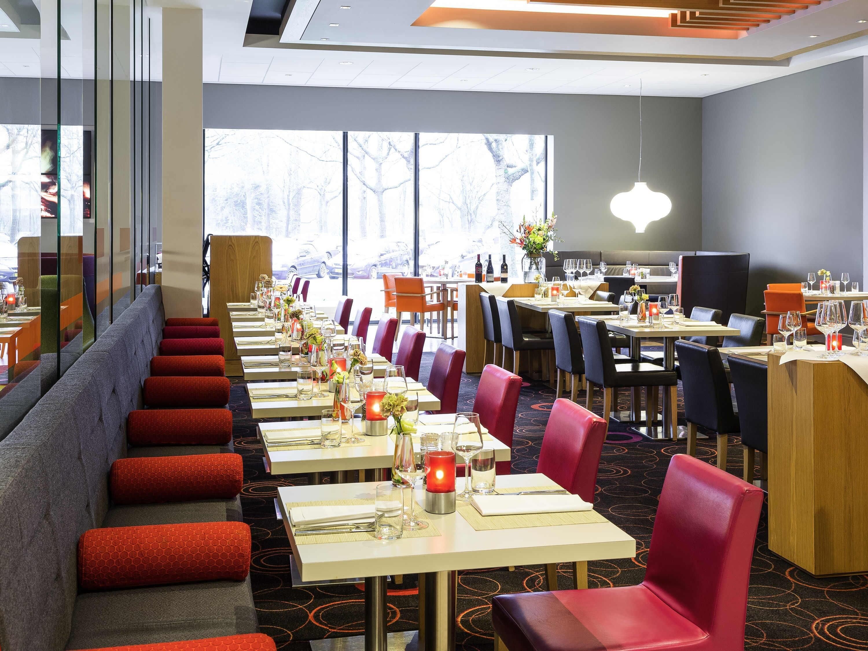 A restaurant with long tables, red and black chairs, and a view of the outside.