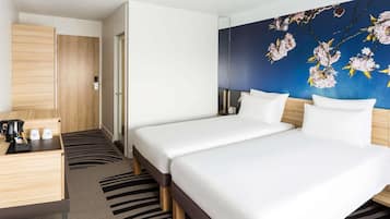 A hotel room with two beds, a wooden desk, a coffee maker, and a wall with a floral mural.