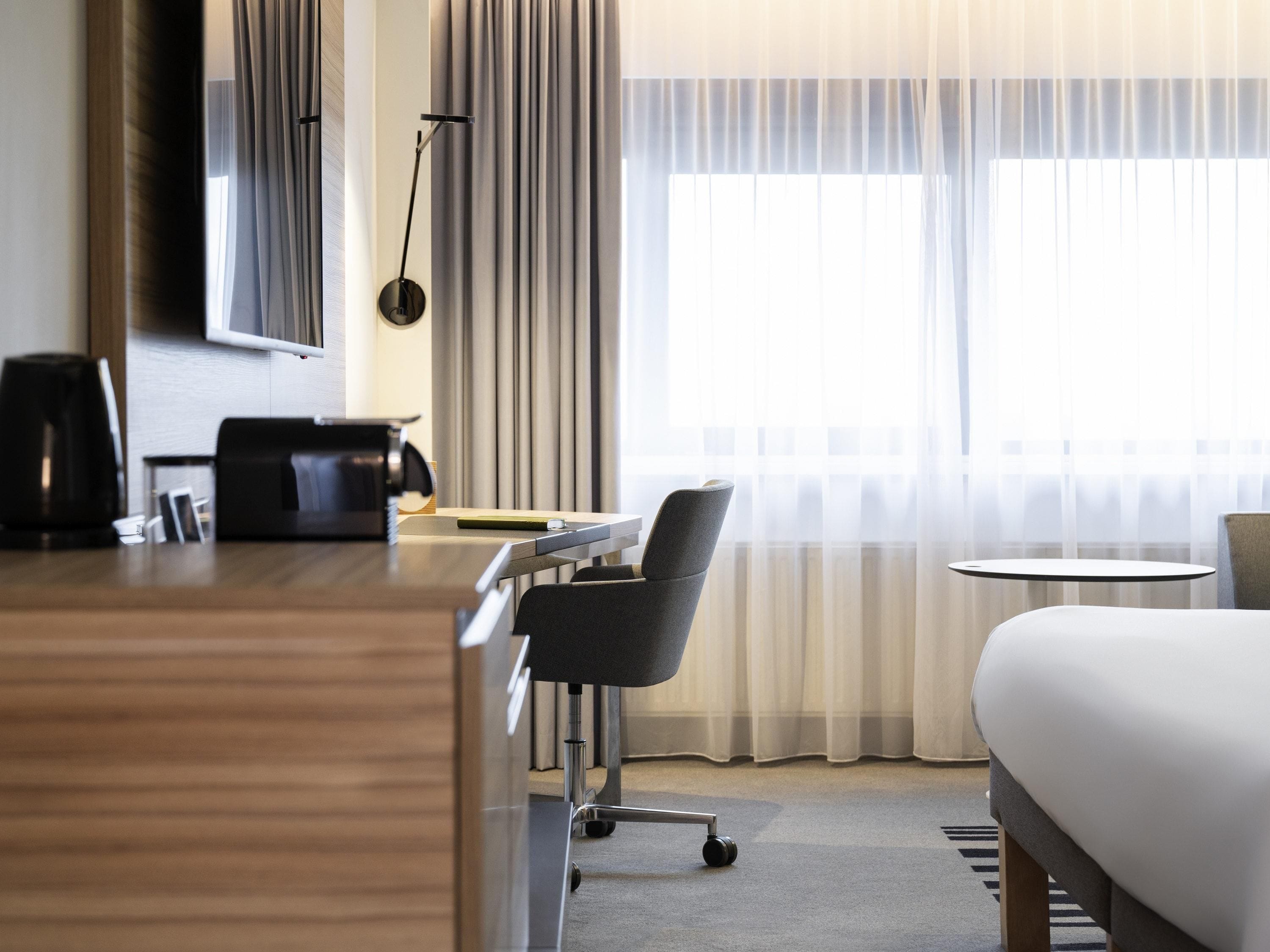 Une chambre d’hôtel comprenant un lit, un bureau avec une chaise, une machine à café et une lampe.