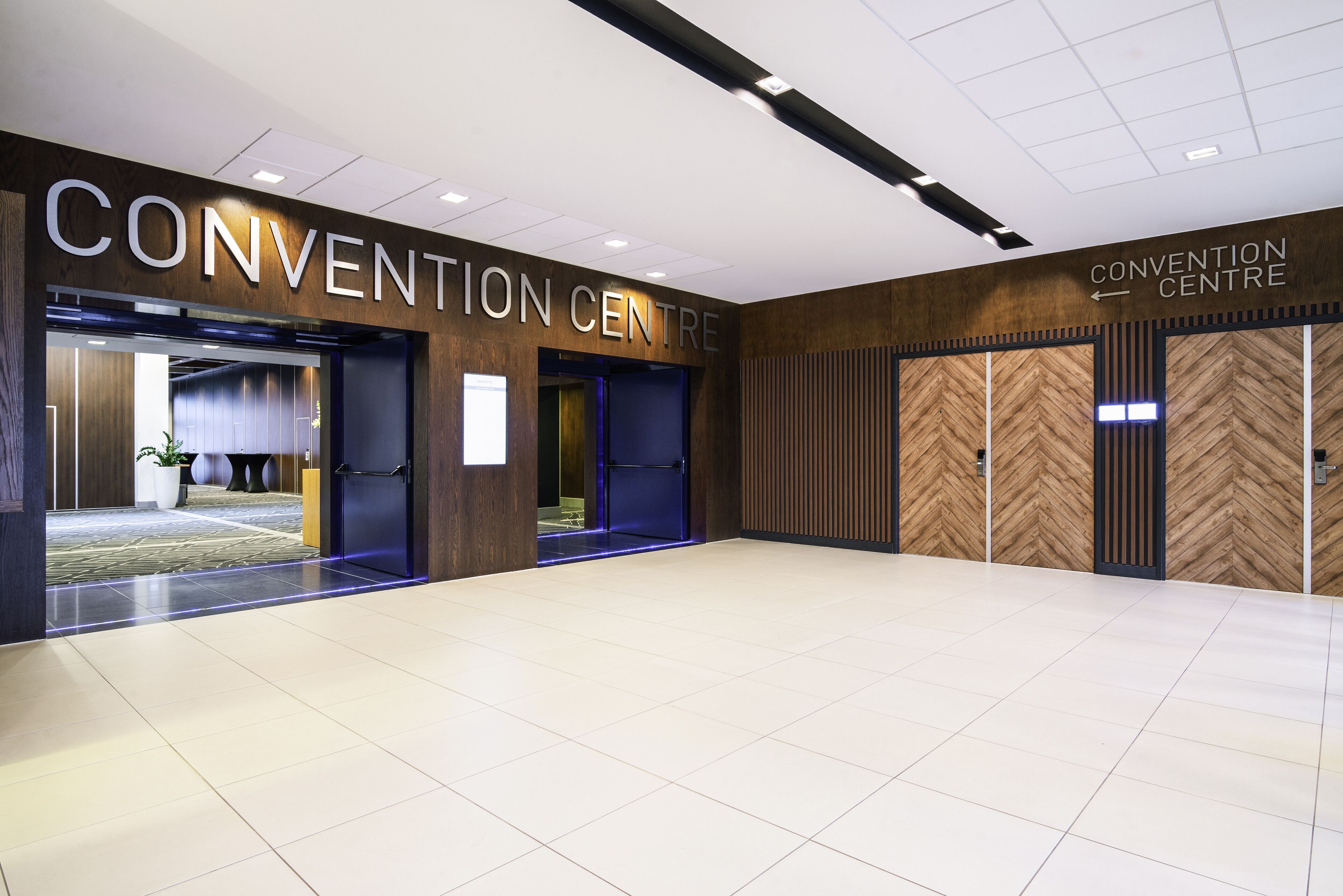 A convention center with a modern interior, featuring a large open space with a tiled floor, wooden paneling on the walls, and a sign indicating the name of the center.