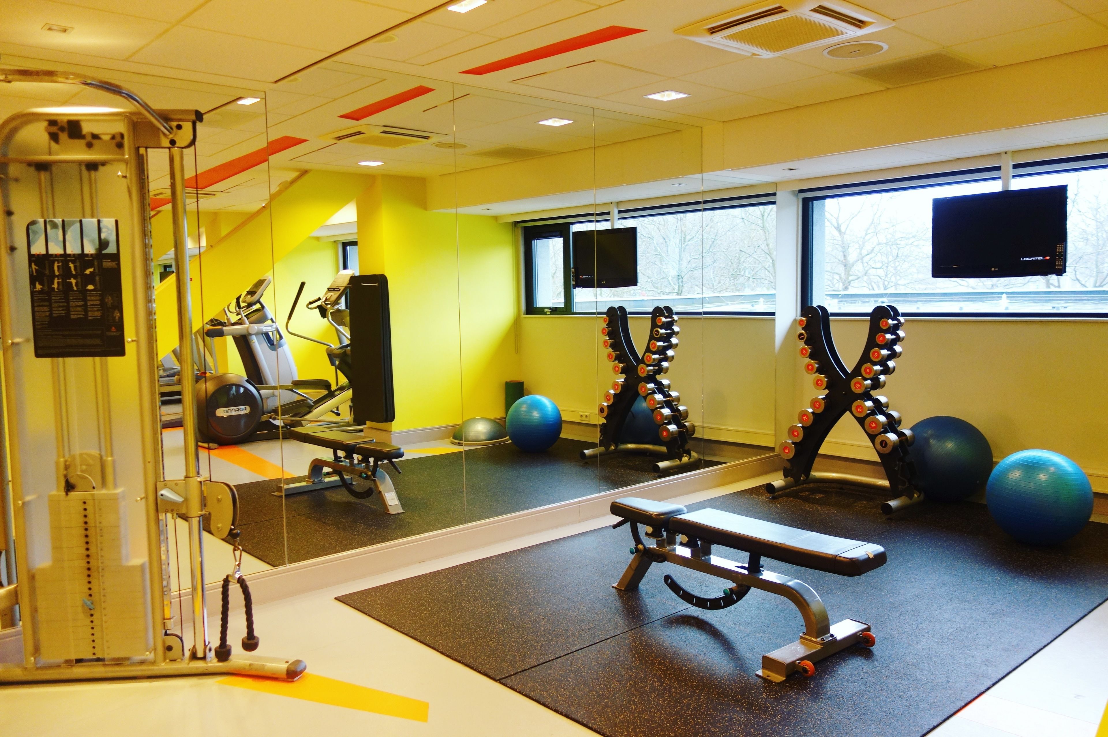Un gimnasio con equipamiento de ejercicio, una banca y pelotas de gimnasia.