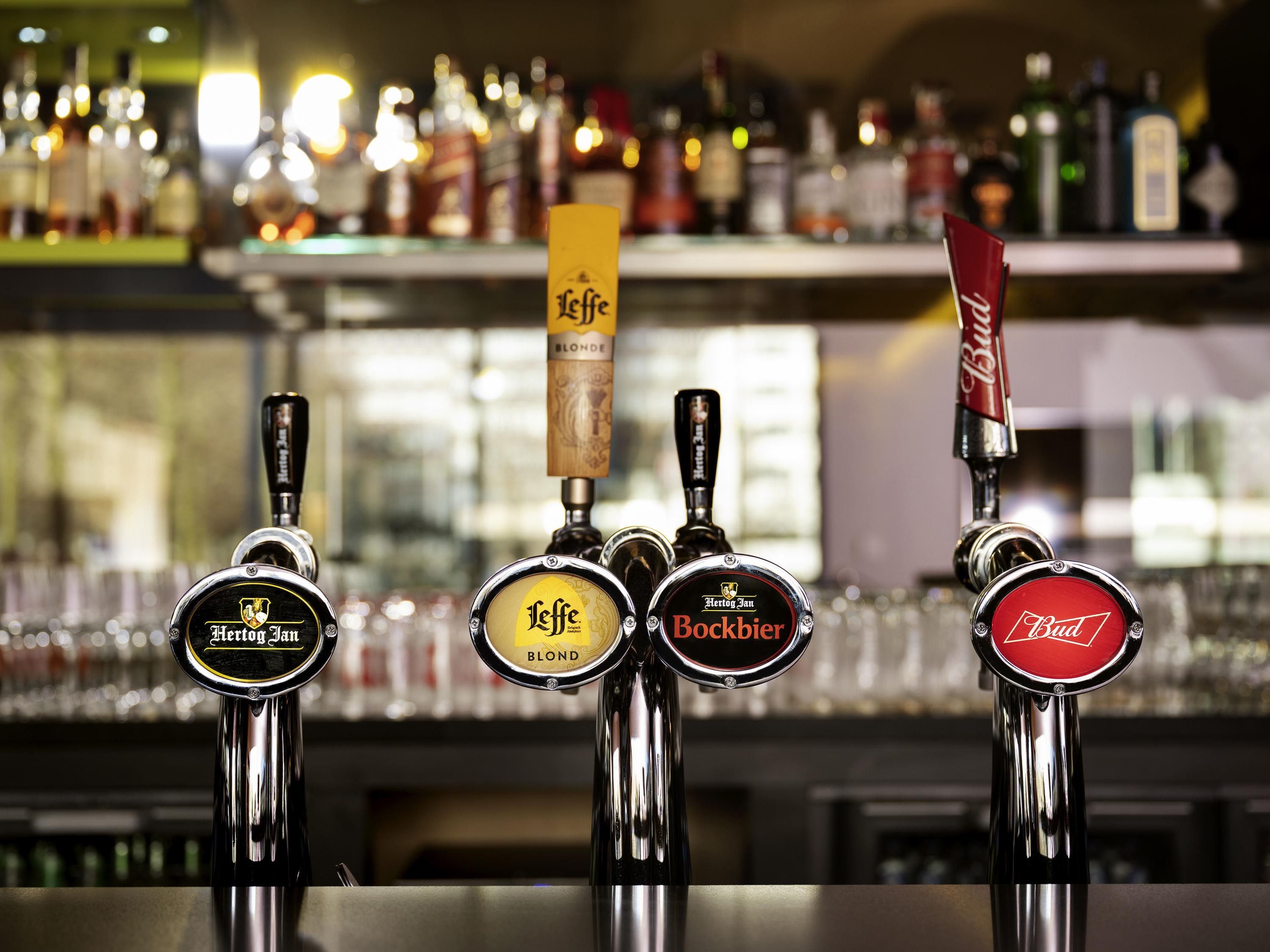 Un bar con varias griferías, incluyendo marcas como Leffe Blonde, Hertog Jan, Bockbier y Budweiser.
