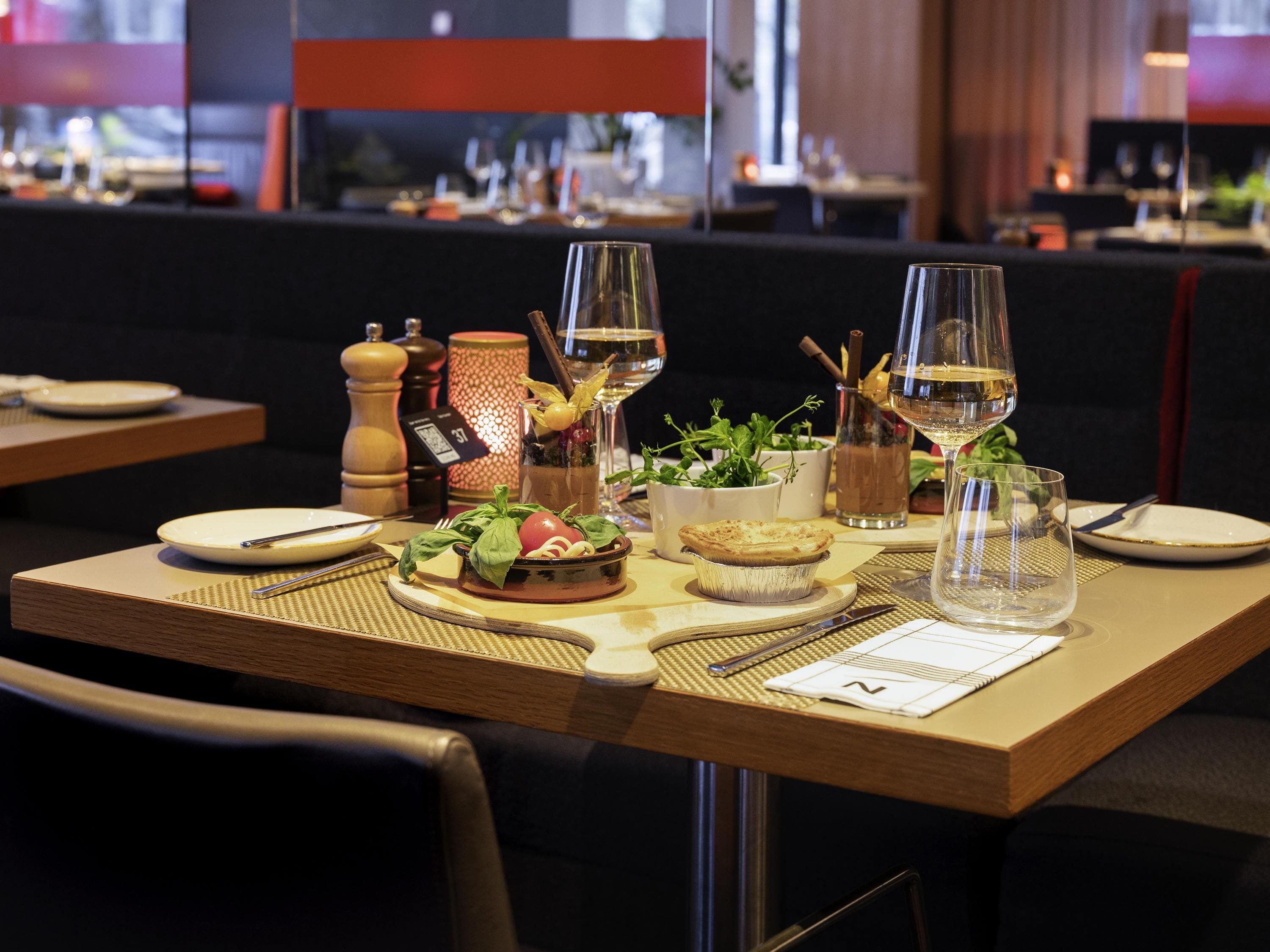 A dining table set with plates, glasses, a menu, and a small plant.
