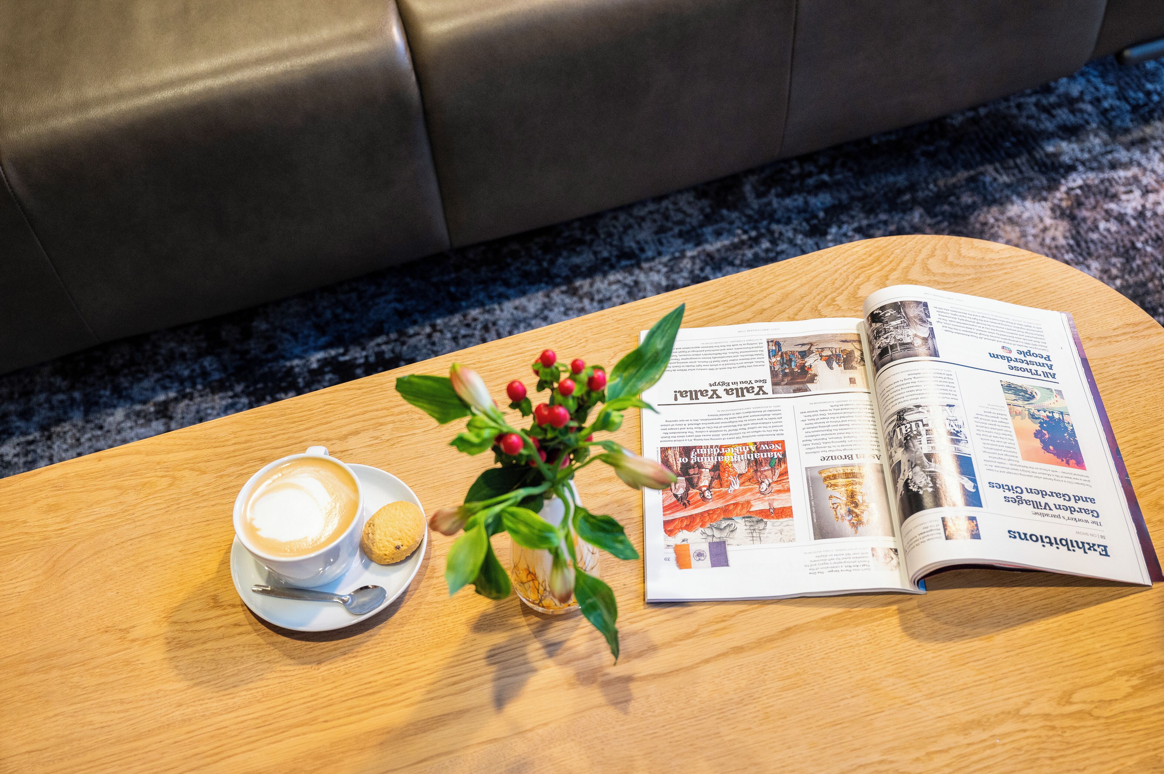 A wooden table with a cup of coffee, a biscuit, and a small potted plant.