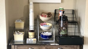 A kitchenette with a coffee machine, bowls, and containers on a wooden counter.