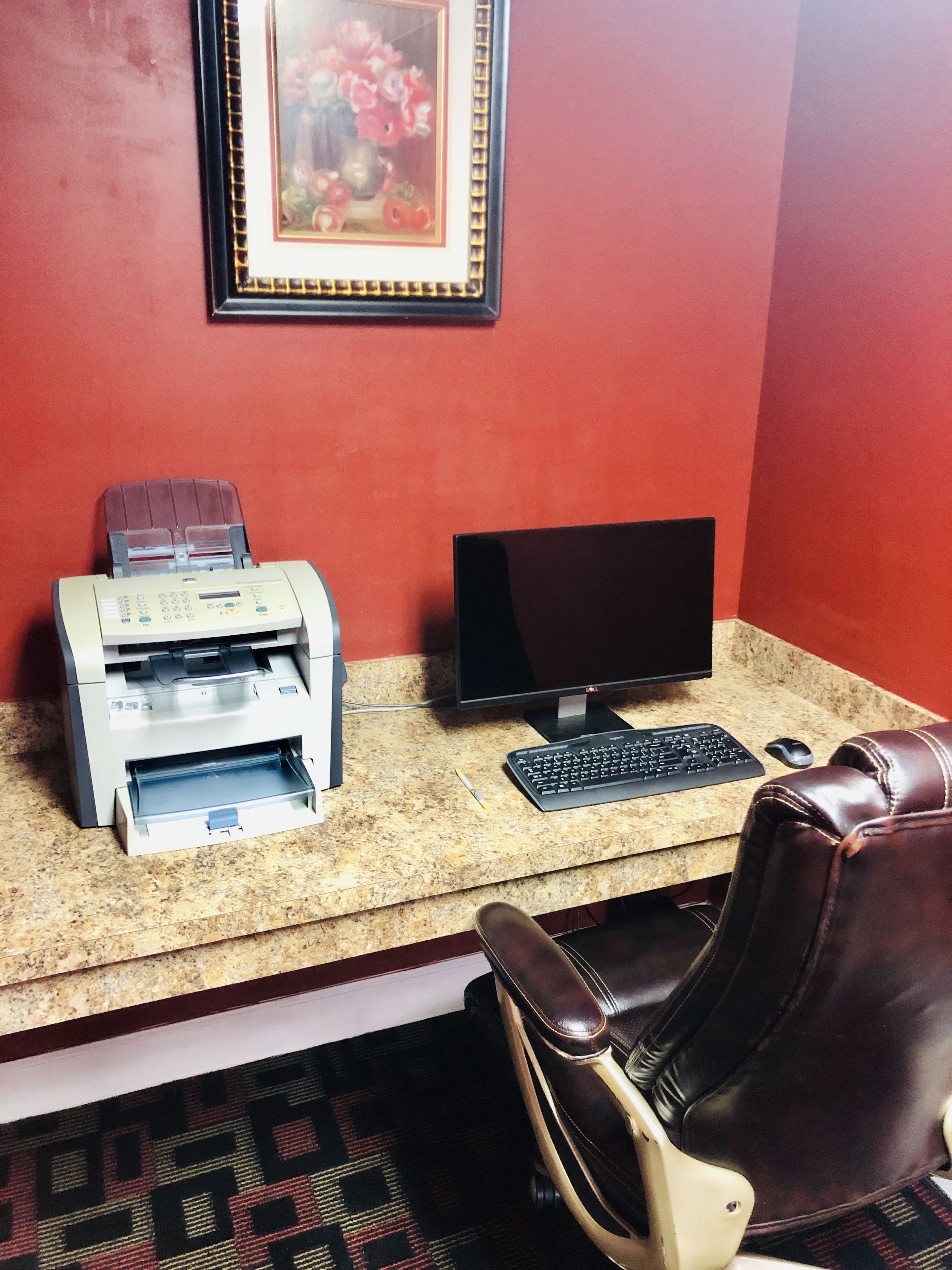A workspace with a printer, computer monitor, keyboard, mouse, and leather chair.