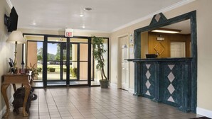 A hotel lobby with a reception desk, an exit sign, and a view of the outdoors.