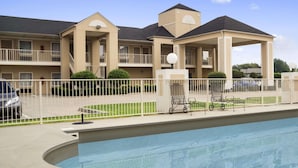 A hotel with a swimming pool, a covered patio, and a fenced parking area.