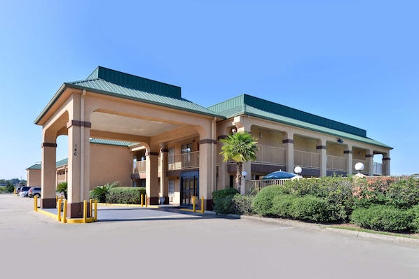 A hotel with a covered entrance, multiple balconies, and a parking lot.
