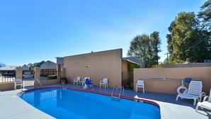 A swimming pool with a clear blue water, surrounded by white lounge chairs and a beige building.