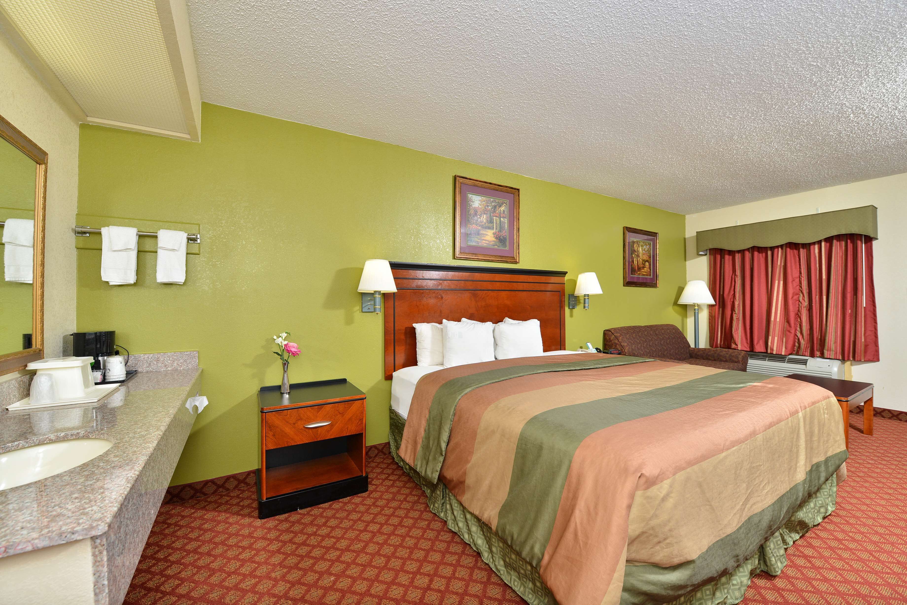 A hotel room with a bed, a vanity with a mirror, a sink, and a nightstand.