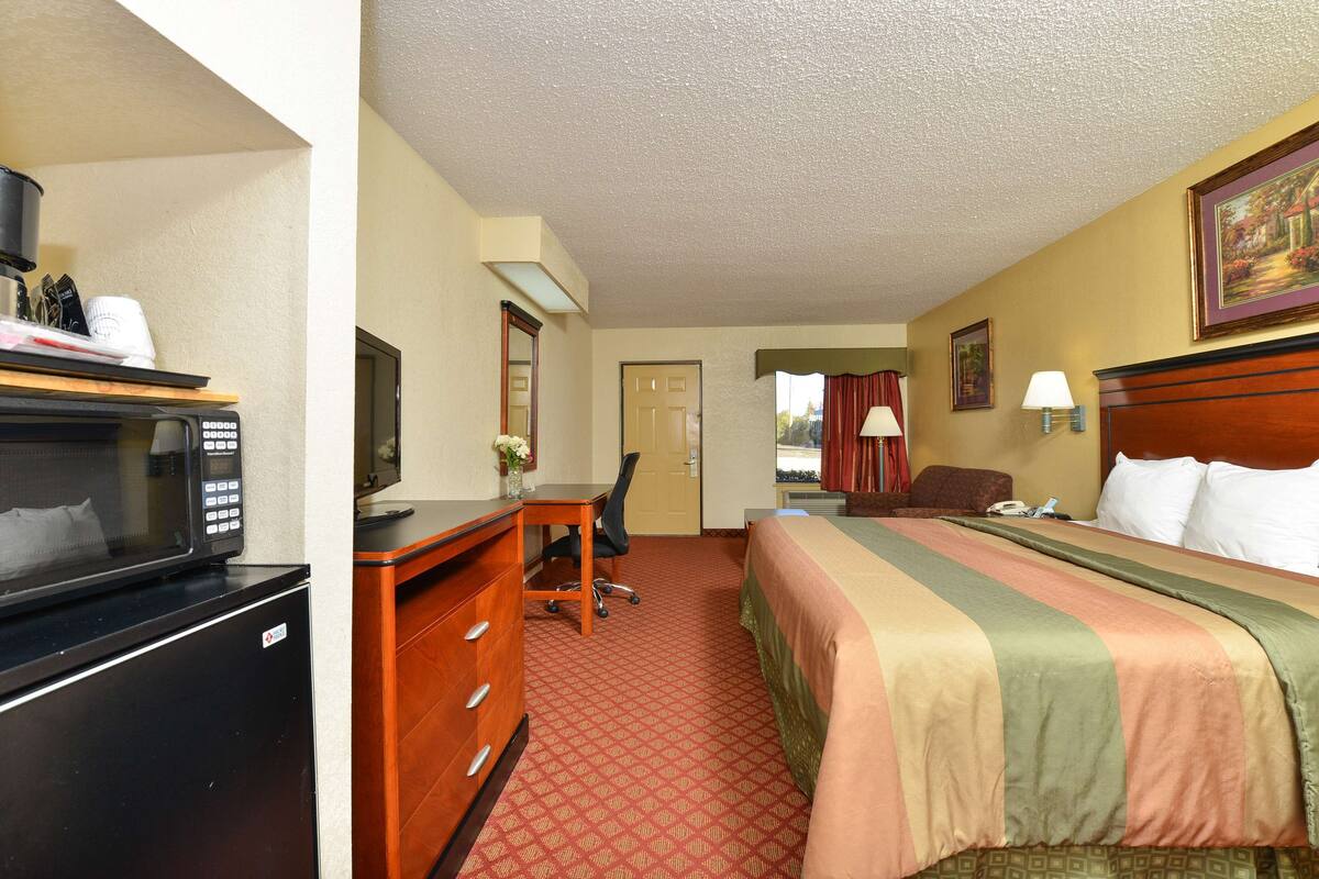 A hotel room with a bed, a desk with a chair, a microwave, a dresser, and a television.