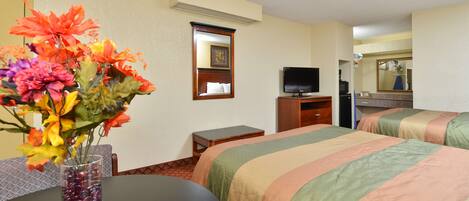 A hotel room with two beds, a TV, a small table with a vase of flowers, and a mirror.