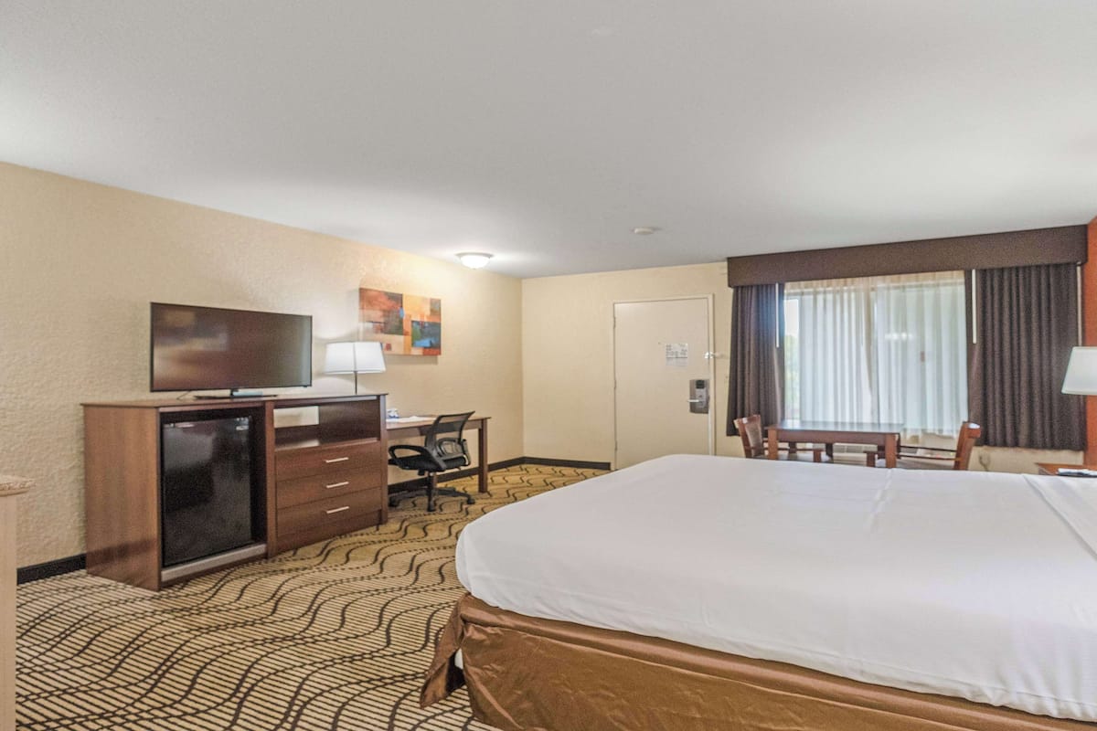 A hotel room with a large bed, a desk with a computer, a television, and a window with curtains.