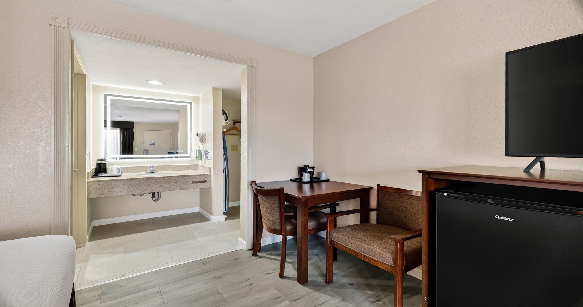A hotel room with a dining area, a small kitchenette, and a television.