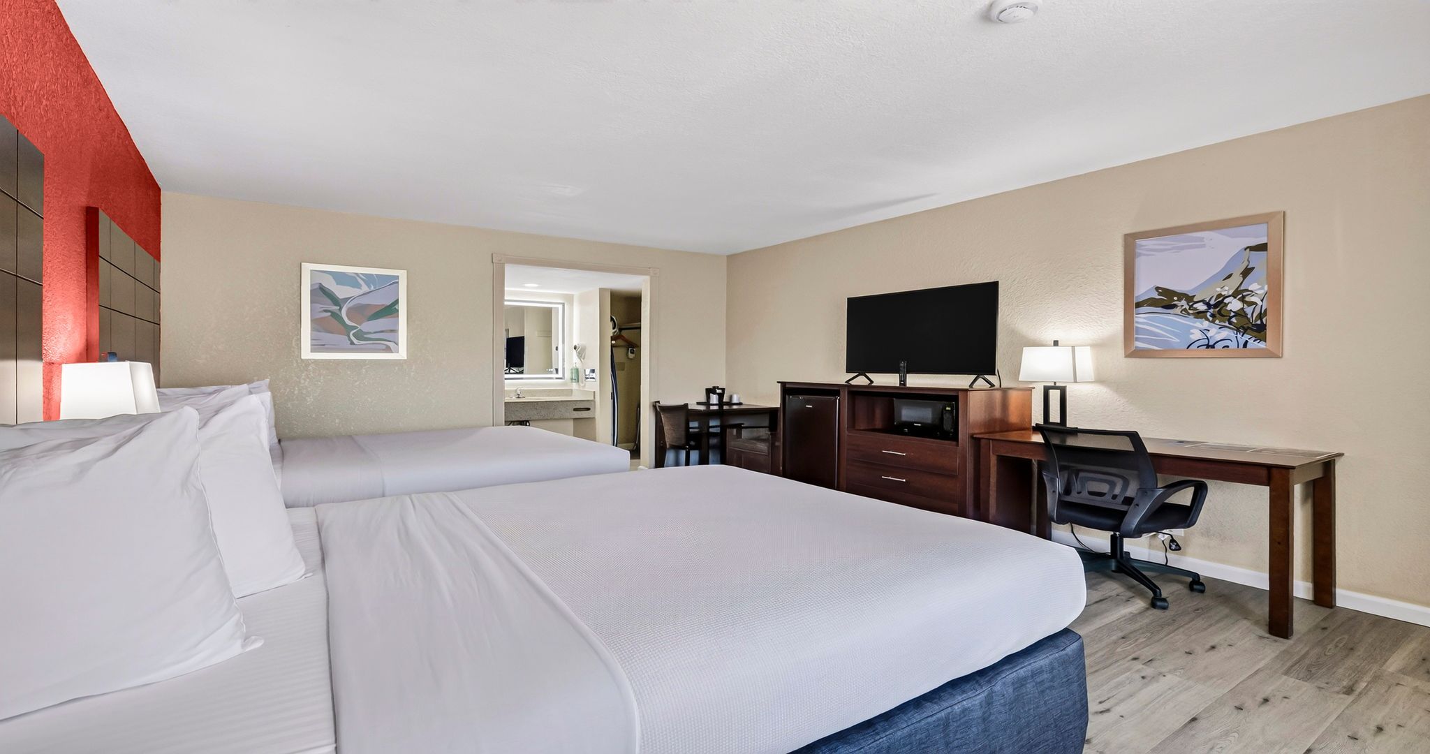 A hotel room with two beds, a desk, a chair, a television, and artwork on the walls.