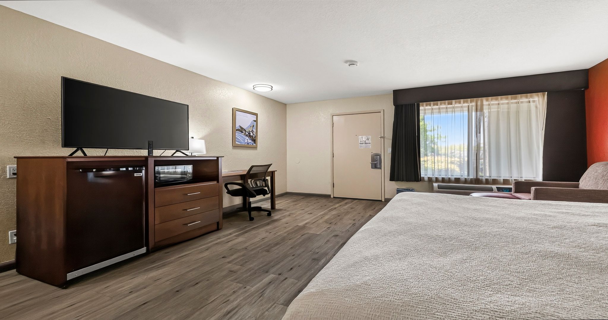 A hotel room with a bed, a desk with a chair, a television, and a door.