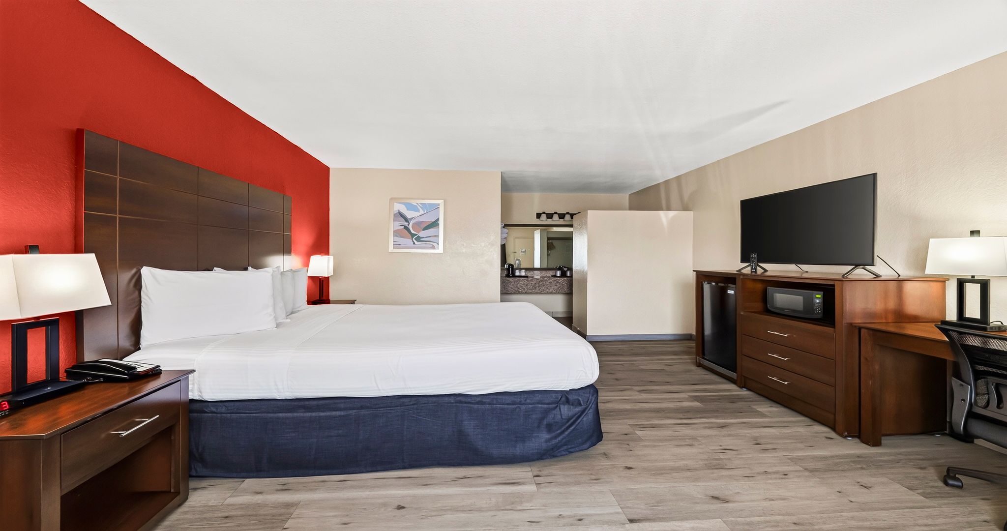Une chambre d’hôtel avec un lit, un bureau, une télévision et une salle de bain visible à travers une porte ouverte.
