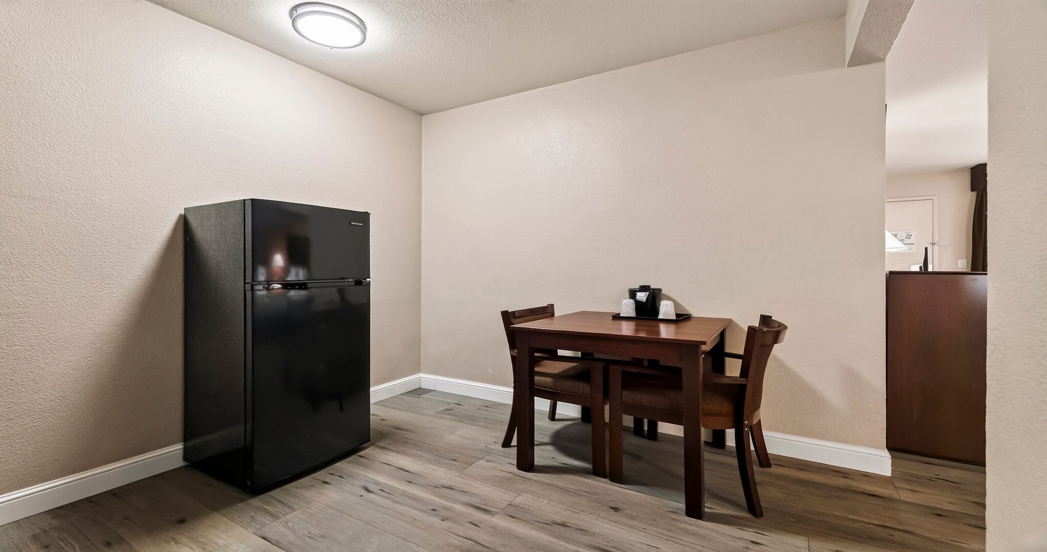 A compact kitchen with a black refrigerator, wooden dining table, and chairs.