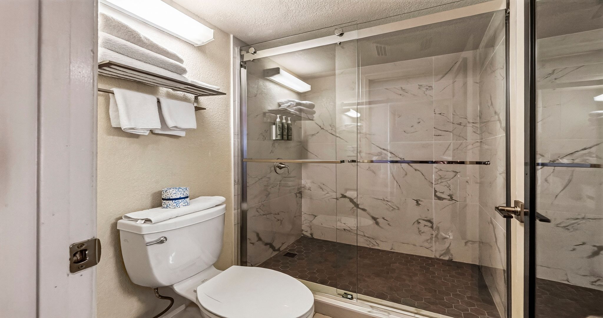 A bathroom with a toilet, a glass shower enclosure, and a towel rack with towels.