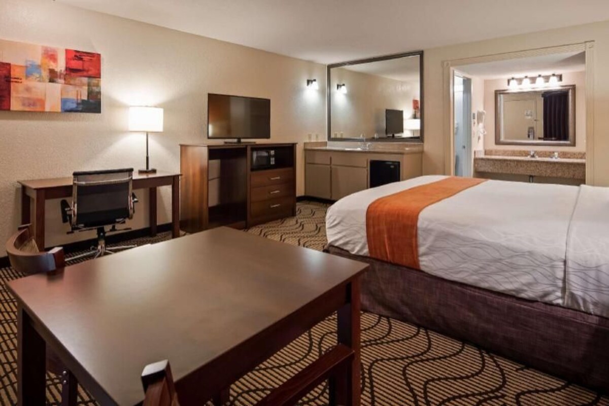 A hotel room with a bed, desk, TV, and a large mirror.