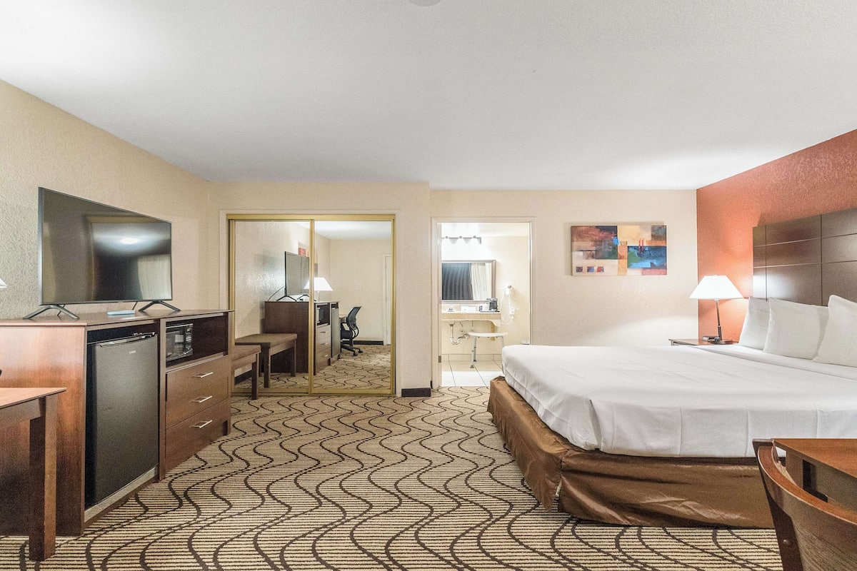 A hotel room with a bed, desk, chair, and a small kitchenette.
