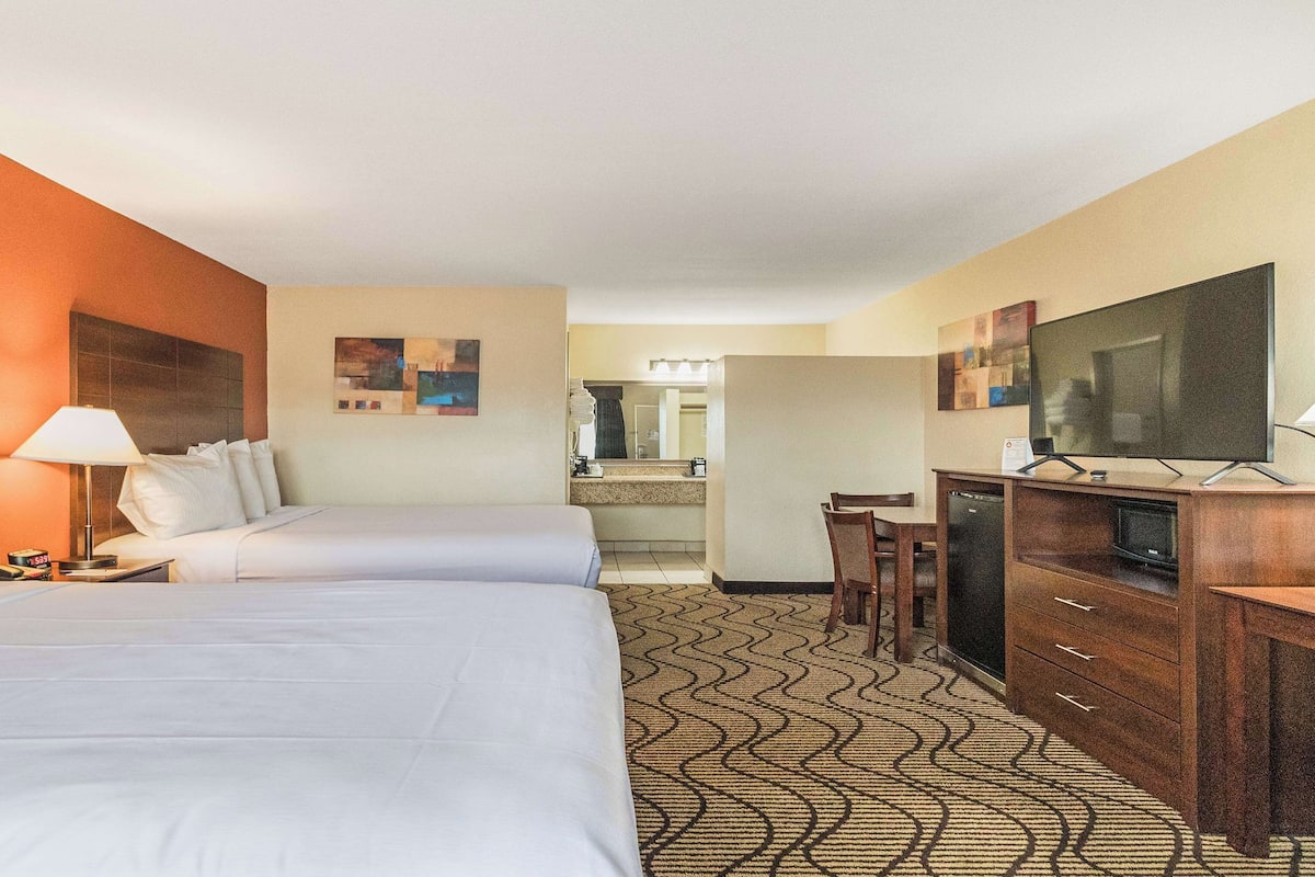 A hotel room with two beds, a desk with a television, a bathroom in the background, and a patterned carpet.