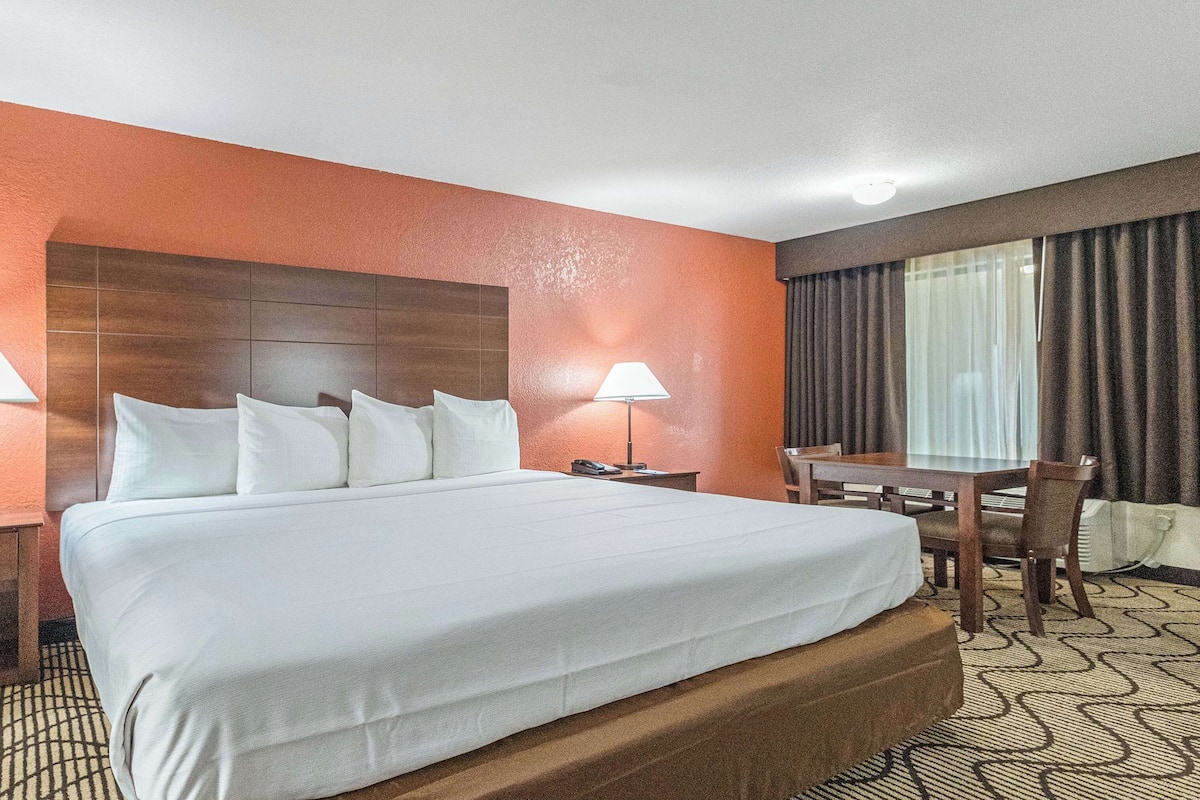 A hotel room with a large bed, two bedside tables with lamps, a wooden desk, and a window with curtains.