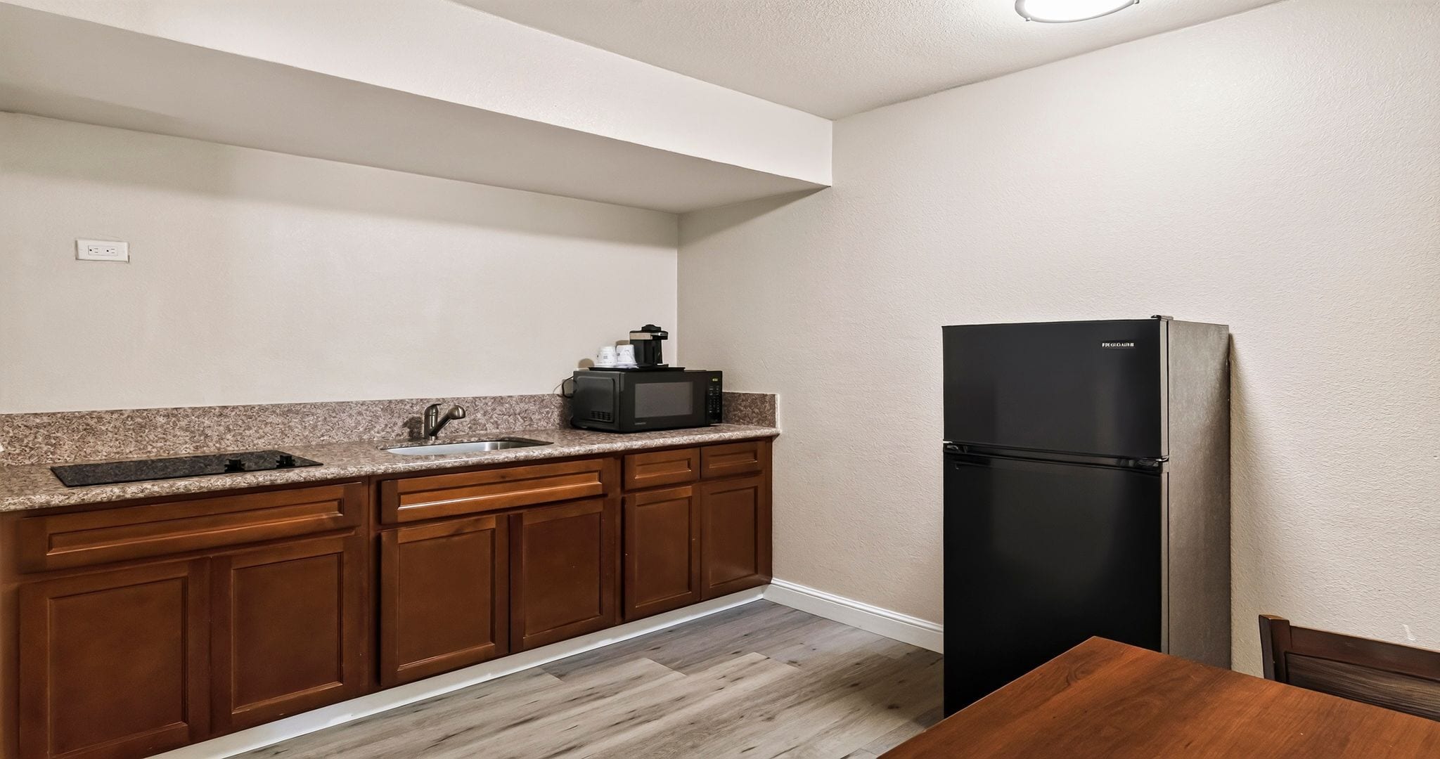 A kitchen with wooden cabinets, a granite countertop, a stainless steel sink, a black refrigerator, and a wooden dining table.