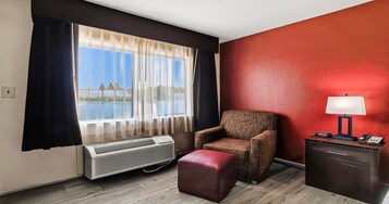 Habitación de hotel con un ventanal grande, una silla, un reposapiés, un escritorio con lámpara y un equipo de aire acondicionado.